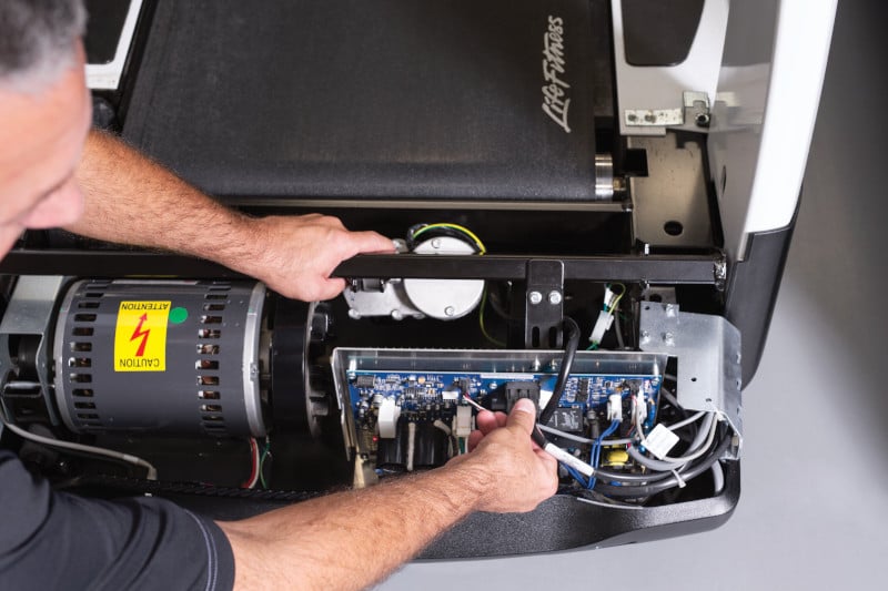 Technician repairing a pre-owned LifeFitness treadmill, ensuring optimal performance and reliability